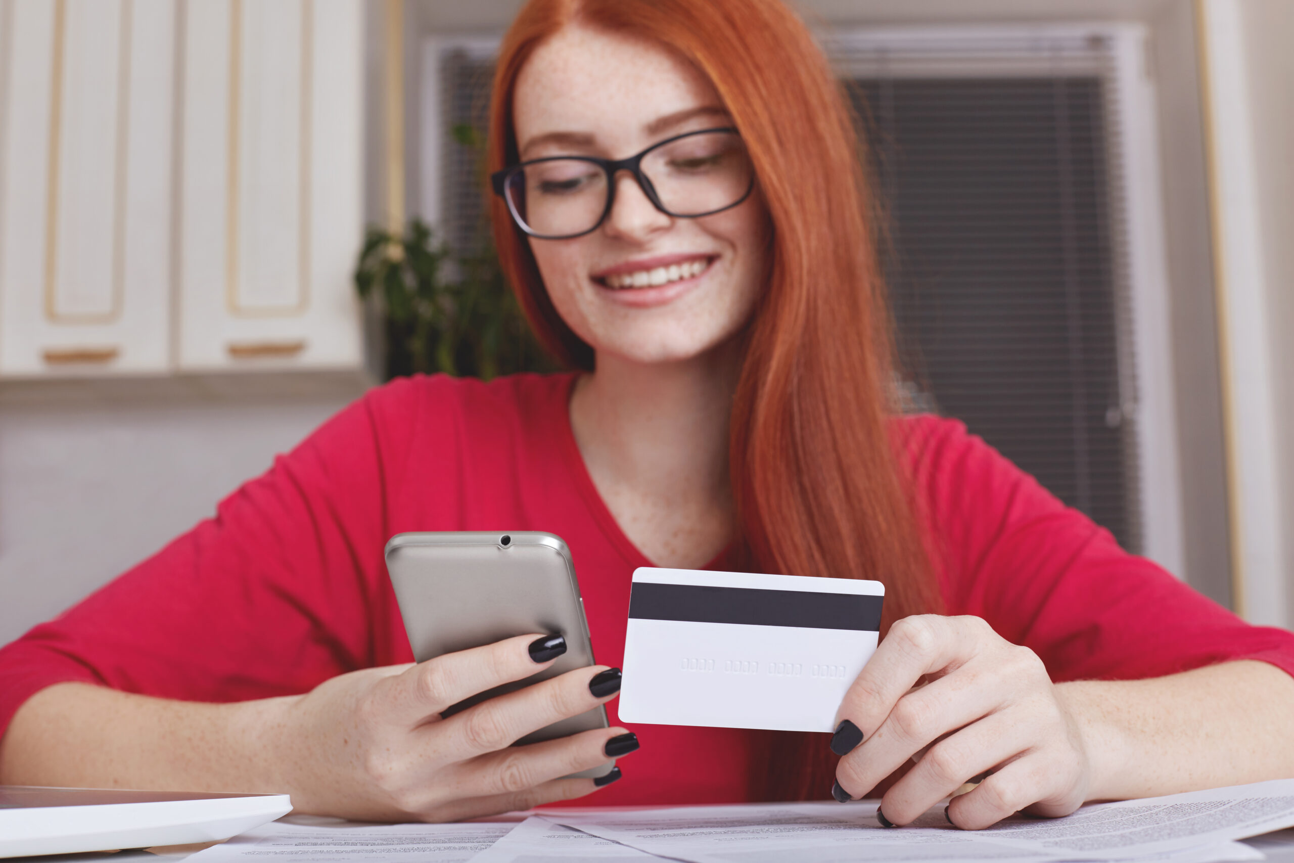 redhaired-pretty-female-model-eyewear-holds-smart-phone-credit-card-scaled.jpg